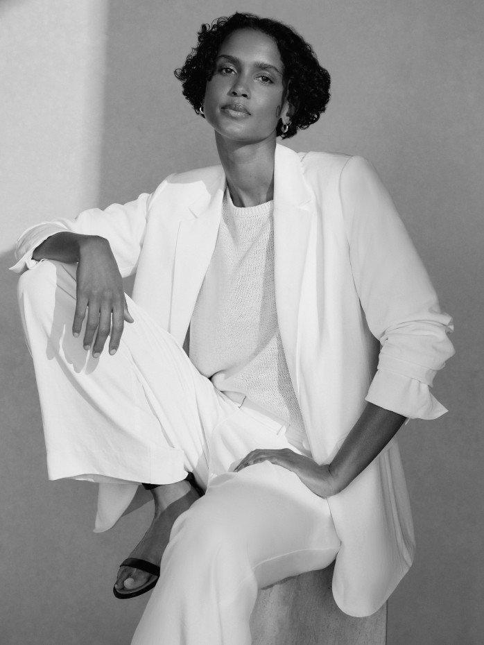 a woman in a white suit sitting on a stool